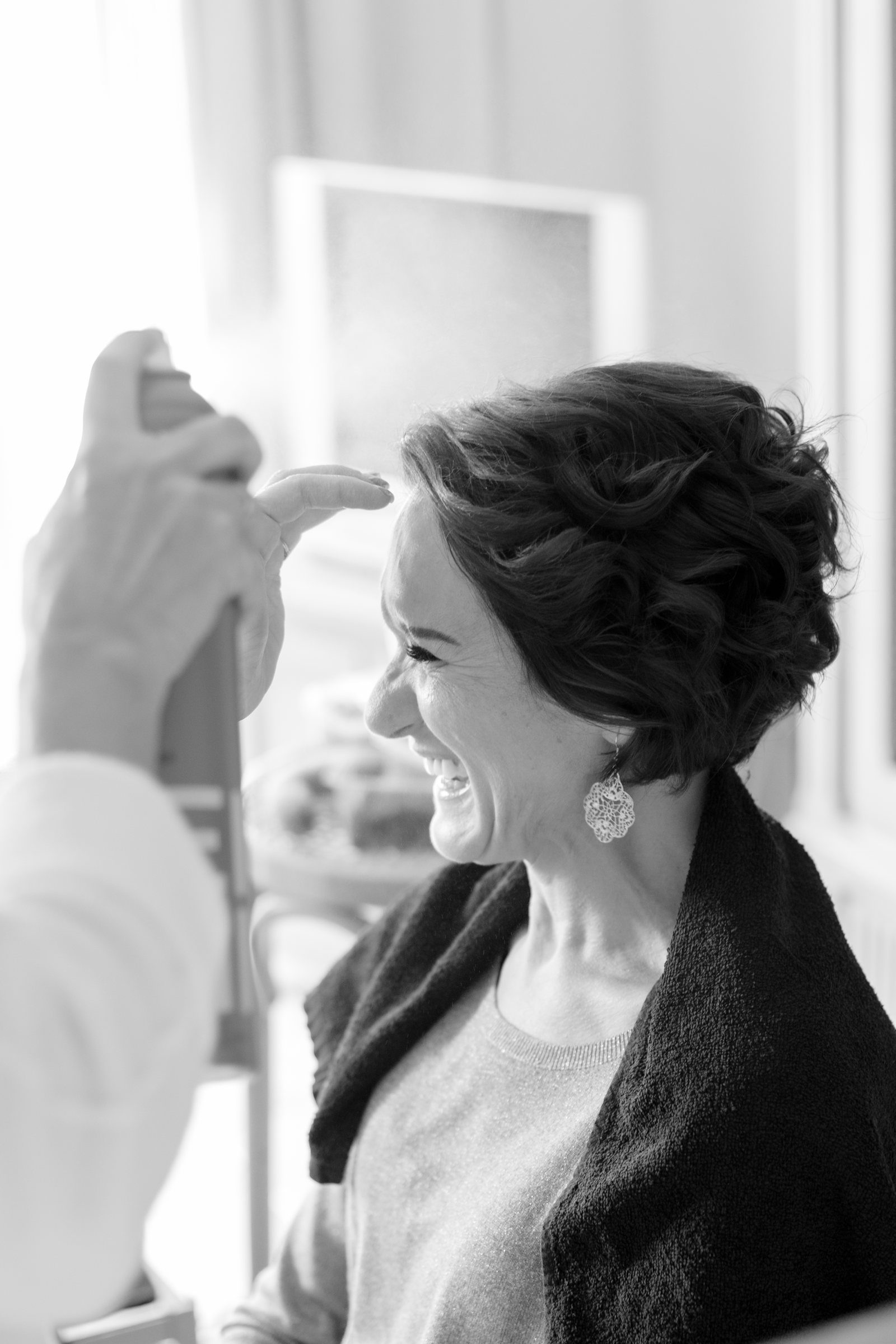 Éclat de rire de la mariée pendant la coiffure, en noir et blanc