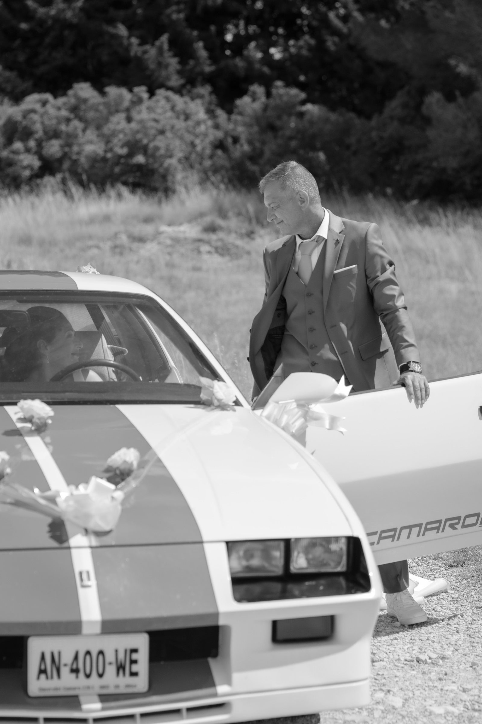 Le marié devant la Chevrolet Camaro, en noir et blanc