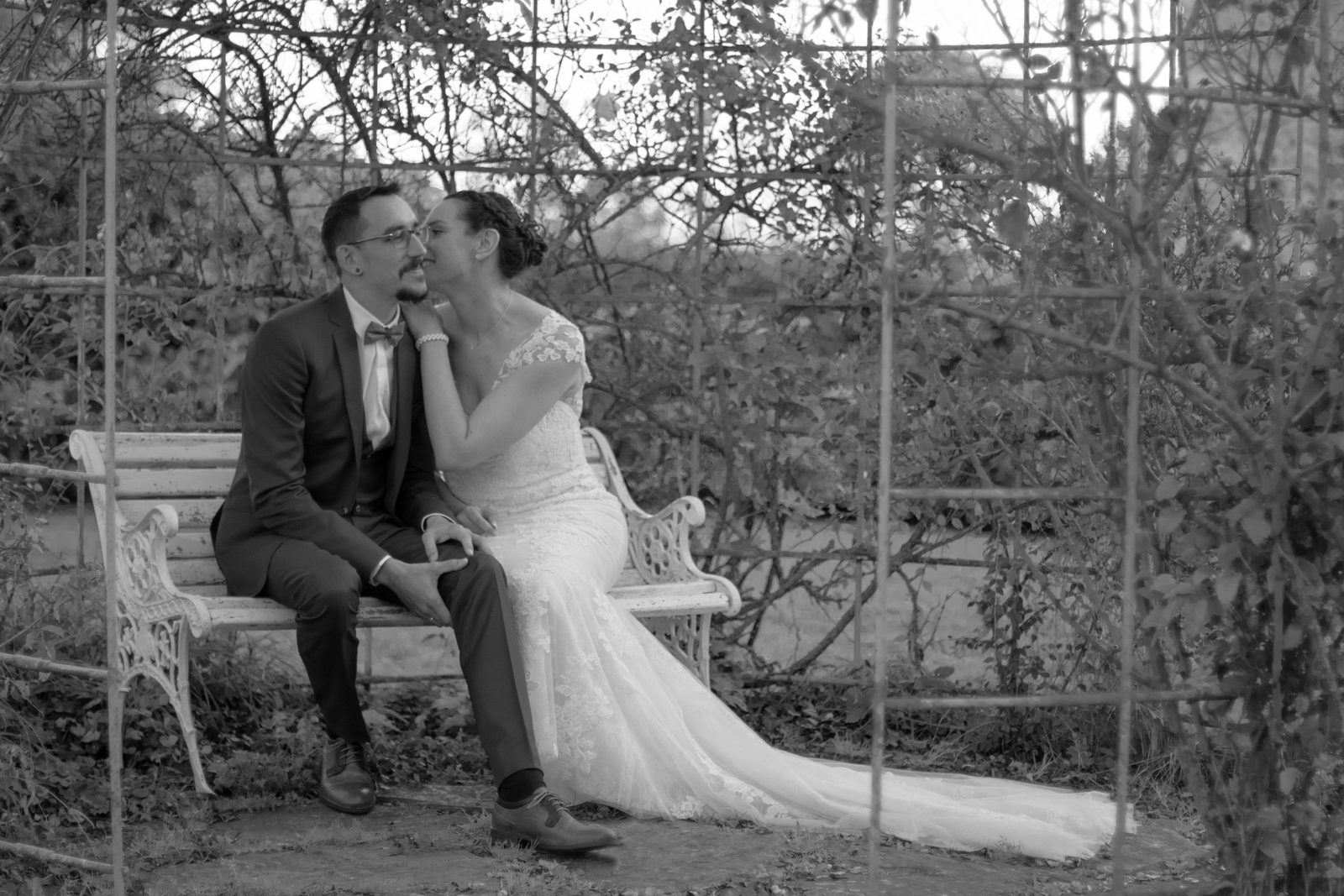 Baiser des mariés sur un banc sous une tonnelle, en noir et blanc