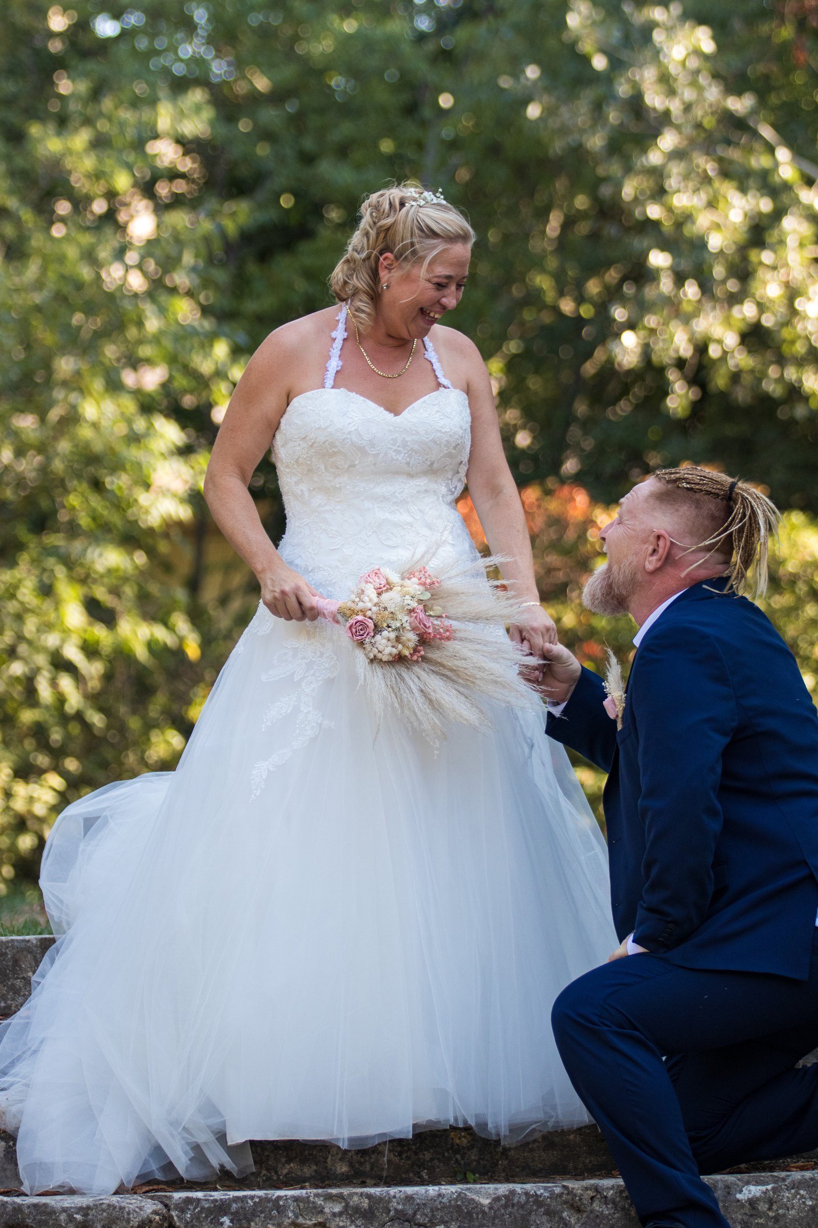 Le marié à genoux devant la mariée qui éclate de rire