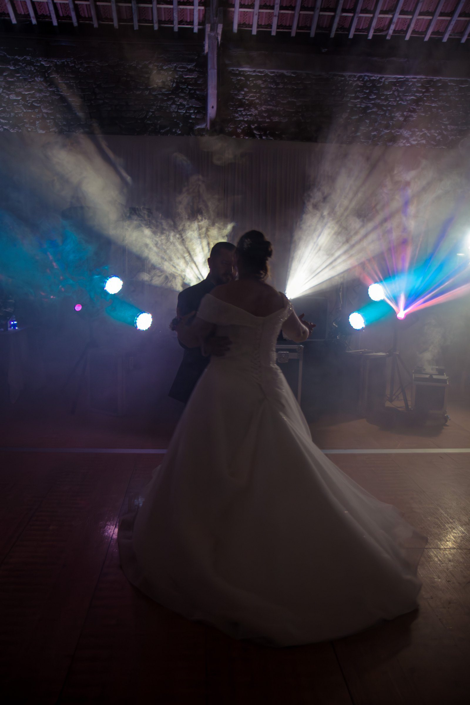 Première danse des mariés dans la fumée et les faisceaux lumineux